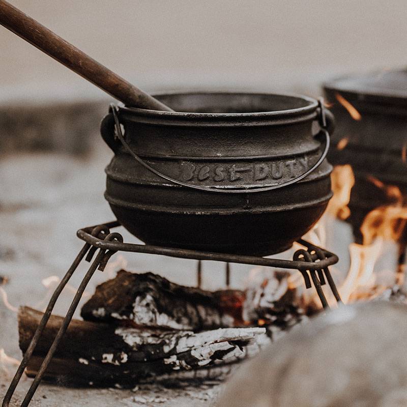 A potjiekos pot from Best Duty sitting on a portable braai stand over a campfire.